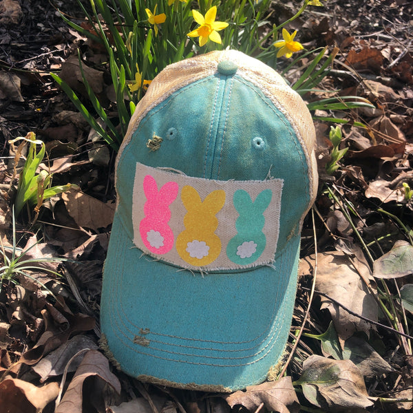 Easter Bunny hat by BohoGroove with pink, yellow, and mint bunny graphics with white flower accents on distressed off-white patch on an ocean blue vintage distressed snapback.
