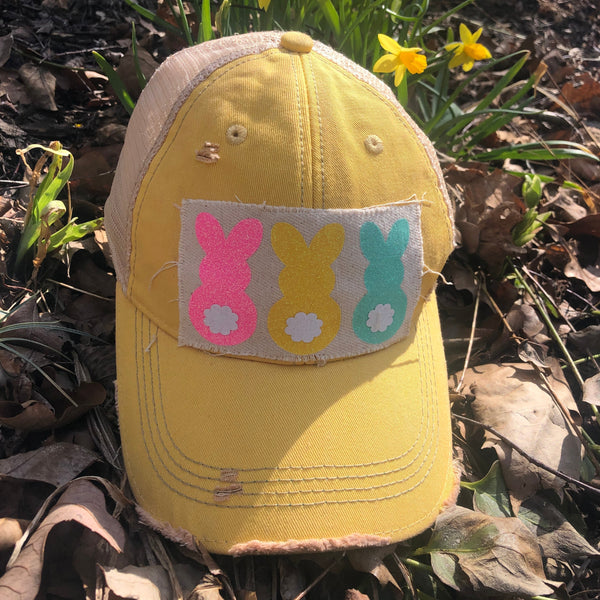 Easter Bunny hat by BohoGroove with pink, yellow, and mint bunny graphics with white flower accents on distressed off-white patch on a yellow vintage distressed snapback.