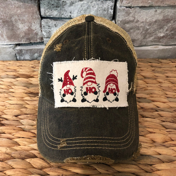 Gnome Ho Ho Ho hat by BohoGroove with three Christmas gnomes wearing red glitter hats and Ho Ho Ho lettering on a distressed off-white patch on a black vintage distressed snapback.