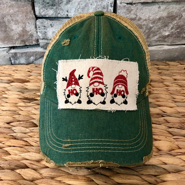 Gnome Ho Ho Ho hat by BohoGroove with three Christmas gnomes wearing red glitter hats and Ho Ho Ho lettering on a distressed off-white patch on a green vintage distressed snapback.