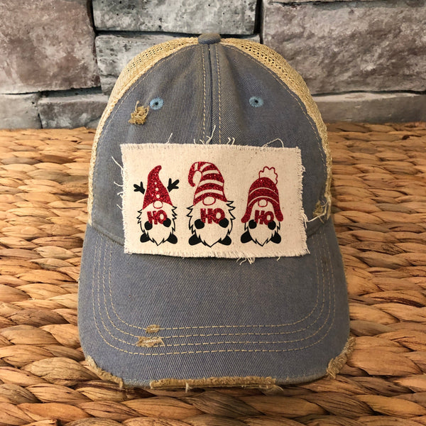 Gnome Ho Ho Ho hat by BohoGroove with three Christmas gnomes wearing red glitter hats and Ho Ho Ho lettering on a distressed off-white patch on a light blue vintage distressed snapback.
