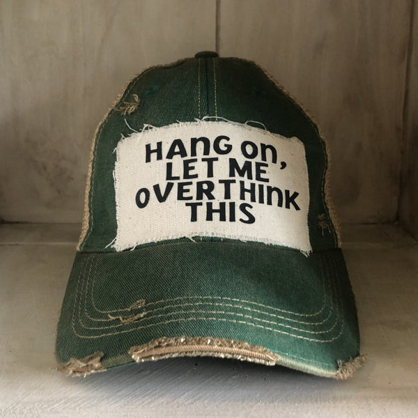 Hang On Let Me Overthink This hat by BohoGroove with black Hang On Let Me Overthink This lettering on a distressed off-white patch on a green vintage distressed snapback trucker hat.