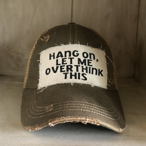 Hang On Let Me Overthink This hat by BohoGroove with black Hang On Let Me Overthink This lettering on a distressed off-white patch on an olive vintage distressed snapback trucker hat.