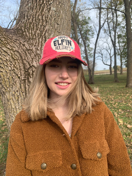 Happy Elfin' Holidays hat by BohoGroove with black lettering and blue snowflake graphics on a distressed off-white custom patch on a pink vintage distressed snapback on model facing forward.