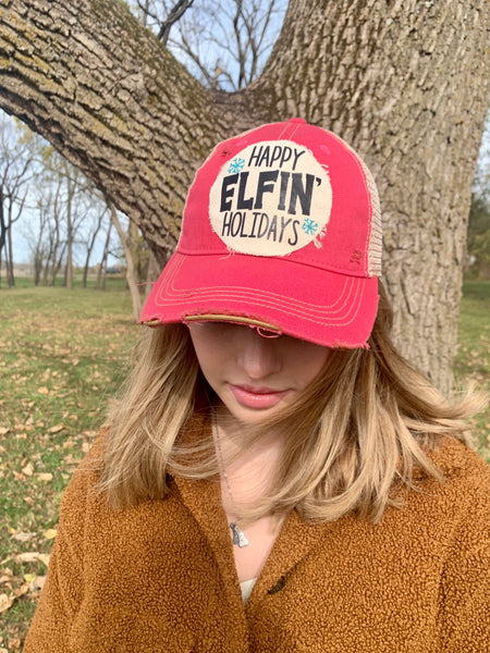 Happy Elfin' Holidays hat by BohoGroove with black lettering and blue snowflake graphics on a distressed off-white custom patch on a pink vintage distressed snapback on model facing down.