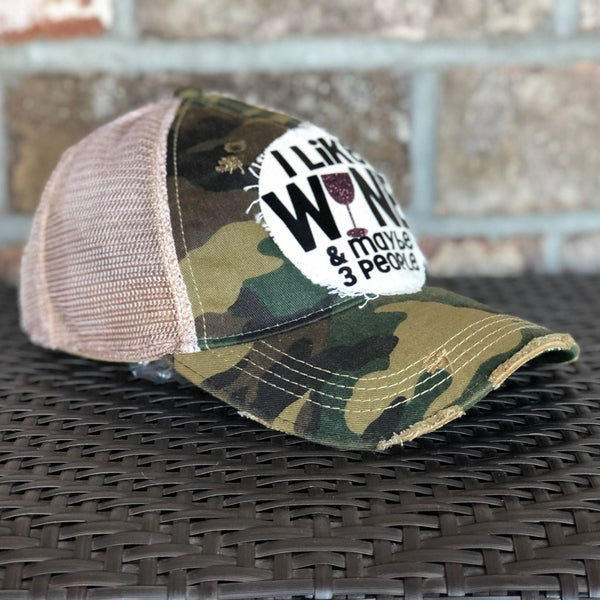 Left side of I Like Wine and Maybe 3 People hat by BohoGroove with black lettering and a glitter wine glass graphic on a distressed off-white patch on a camo vintage distressed snapback.