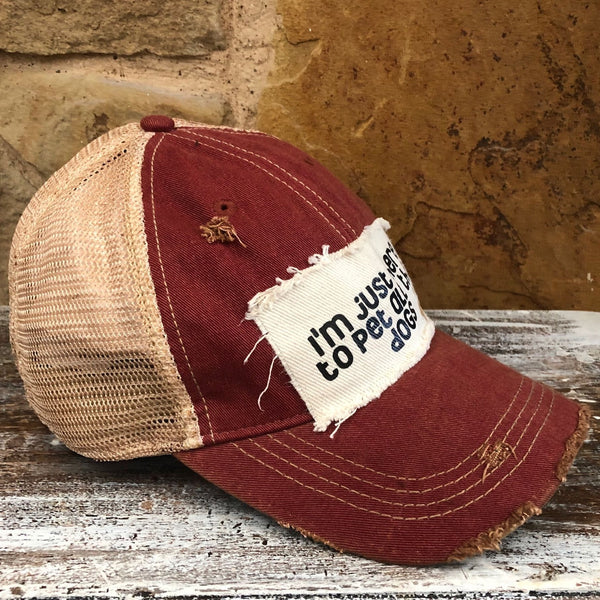 I'm Just Here to Pet All the Dogs hat by BohoGroove with black I'm Just Here to Pet All the Dogs lettering and paw print graphic on a distressed off-white patch on a brick red vintage distressed snapback left side.