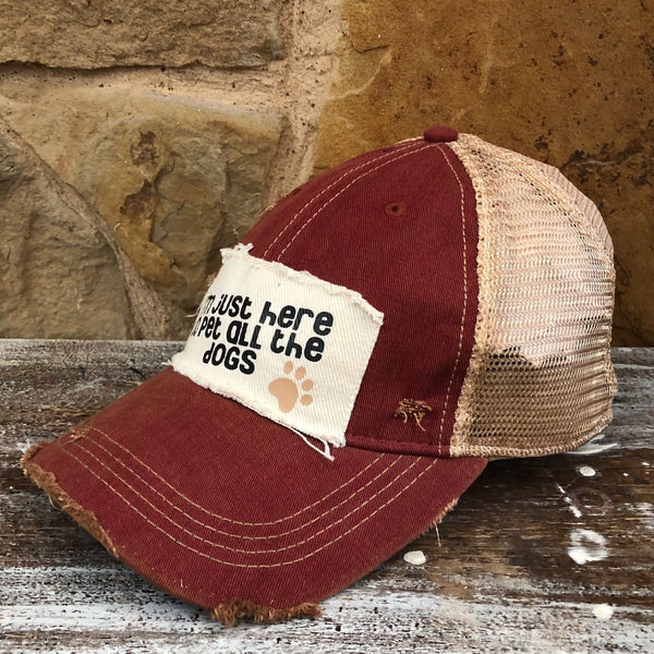 I'm Just Here to Pet All the Dogs hat by BohoGroove with black I'm Just Here to Pet All the Dogs lettering and paw print graphic on a distressed off-white patch on a brick red vintage distressed snapback right side.