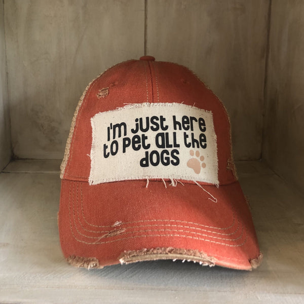 I'm Just Here to Pet All the Dogs hat by BohoGroove with black I'm Just Here to Pet All the Dogs lettering and paw print graphic on a distressed off-white patch on an orange vintage distressed snapback.