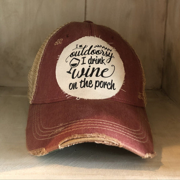 I'm Outdoorsy I Drink Wine on the Porch hat by BohoGroove with black lettering and wine glass graphic on a distressed off-white patch on a brick red vintage distressed snapback trucker hat.