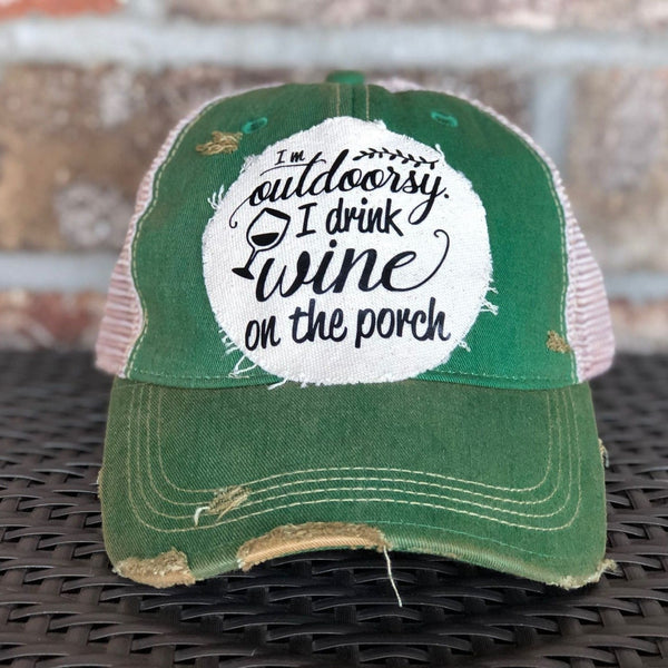 I'm Outdoorsy I Drink Wine on the Porch hat by BohoGroove with black lettering and wine glass graphic on a distressed off-white patch on a green vintage distressed snapback trucker hat.