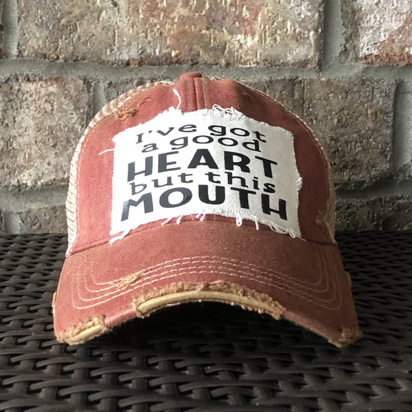 I've Got a Good Heart, but This Mouth hat by BohoGroove with black lettering on a distressed off-white patch on a brick red vintage distressed snapback trucker hat.