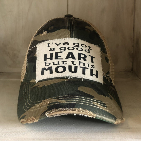 I've Got a Good Heart, but This Mouth hat by BohoGroove with black lettering on a distressed off-white patch on a camo vintage distressed snapback trucker hat.
