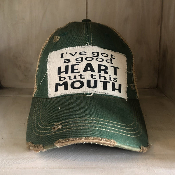 I've Got a Good Heart, but This Mouth hat by BohoGroove with black lettering on a distressed off-white patch on a green vintage distressed snapback trucker hat.