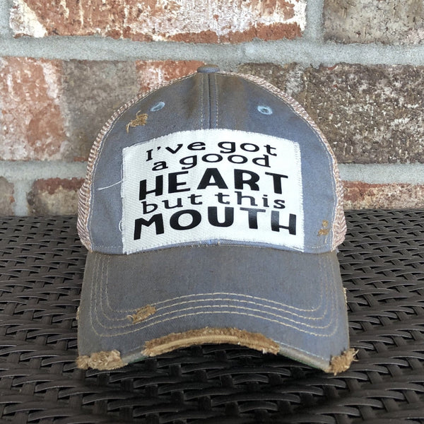 I've Got a Good Heart, but This Mouth hat by BohoGroove with black lettering on a distressed off-white patch on a light blue vintage distressed snapback trucker hat.