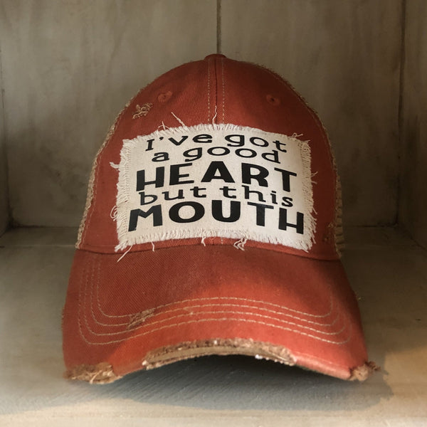 I've Got a Good Heart, but This Mouth hat by BohoGroove with black lettering on a distressed off-white patch on an orange vintage distressed snapback trucker hat.
