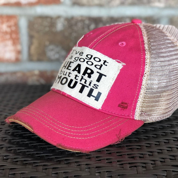 Right side view of I've Got a Good Heart, but This Mouth hat by BohoGroove with black lettering on a distressed off-white patch on a pink vintage distressed snapback trucker hat.
