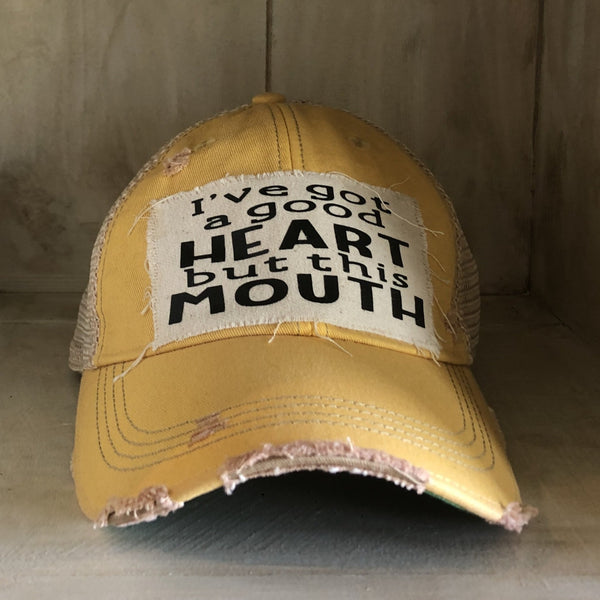 I've Got a Good Heart, but This Mouth hat by BohoGroove with black lettering on a distressed off-white patch on a yellow vintage distressed snapback trucker hat.