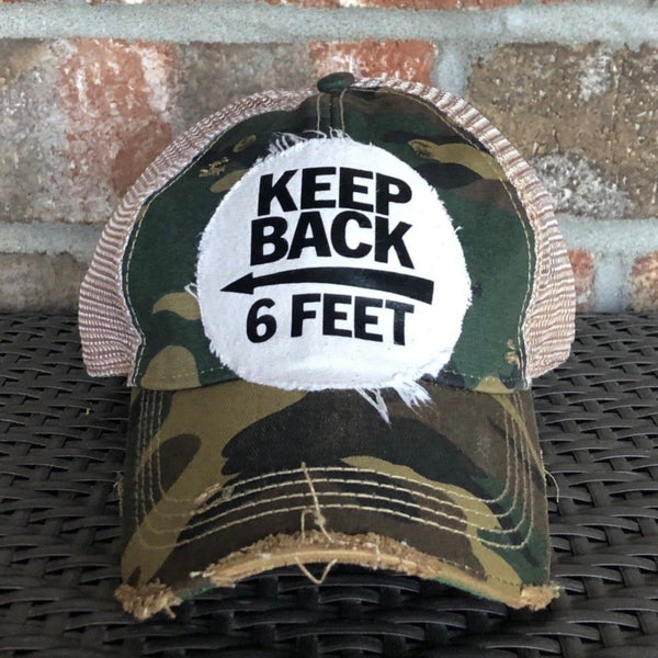Keep Back 6 Feet hat by BohoGroove with black lettering and arrow graphic on a distressed off-white patch on a camo vintage distressed snapback trucker hat.