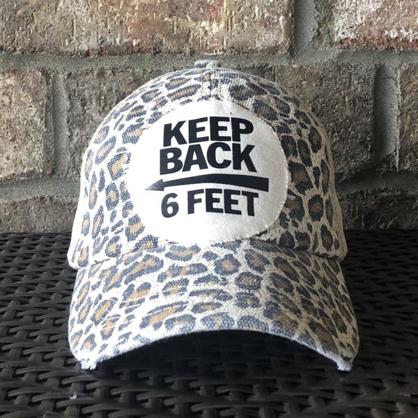 Keep Back 6 Feet hat by BohoGroove with black lettering and arrow graphic on a distressed off-white patch on a leopard vintage distressed snapback trucker hat.