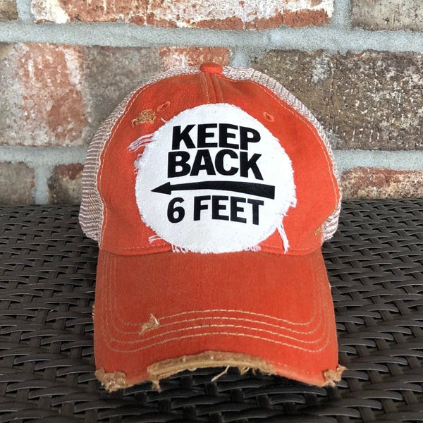 Keep Back 6 Feet hat by BohoGroove with black lettering and arrow graphic on a distressed off-white patch on an orange vintage distressed snapback trucker hat.