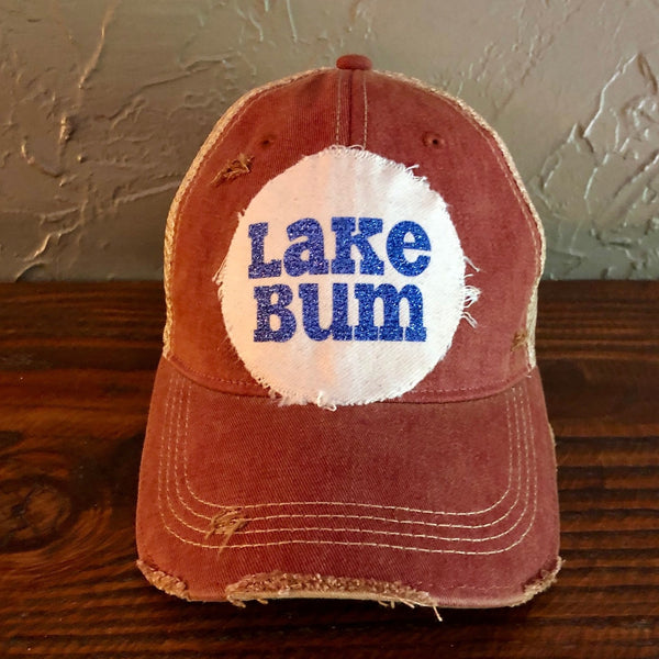 Lake Bum hat by BohoGroove with blue glitter Lake Bum lettering on distressed off-white patch on a brick red vintage distressed snapback.