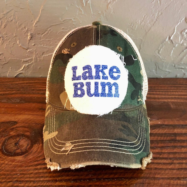 Lake Bum hat by BohoGroove with blue glitter Lake Bum lettering on distressed off-white patch on a camo vintage distressed snapback.