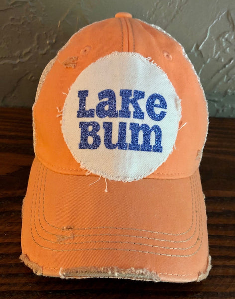 Lake Bum hat by BohoGroove with blue glitter Lake Bum lettering on distressed off-white patch on a sherbet vintage distressed snapback.