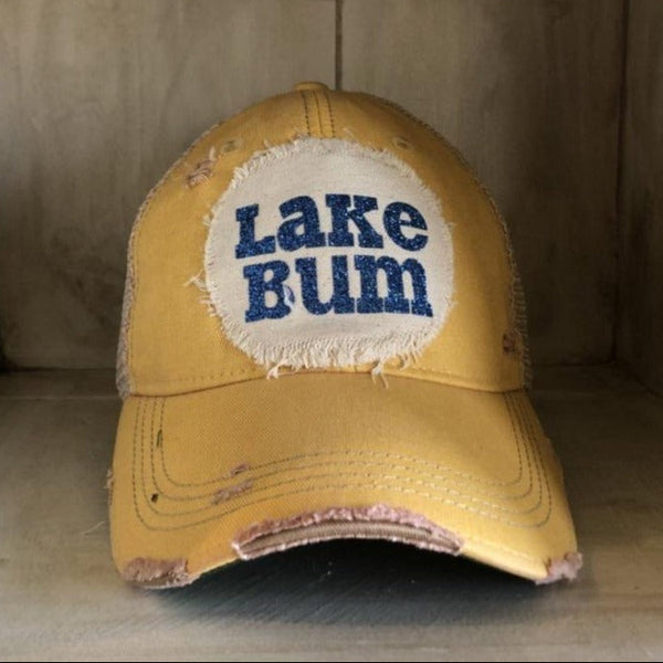Lake Bum hat by BohoGroove with blue glitter Lake Bum lettering on distressed off-white patch on a yellow vintage distressed snapback.