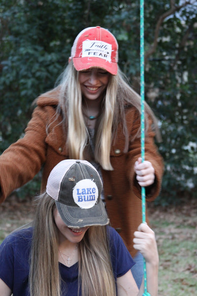 Two women wearing BohoGroove vintage distressed snapback hats on a swing featuring Lake Bum and Faith Over Fear patch designs.