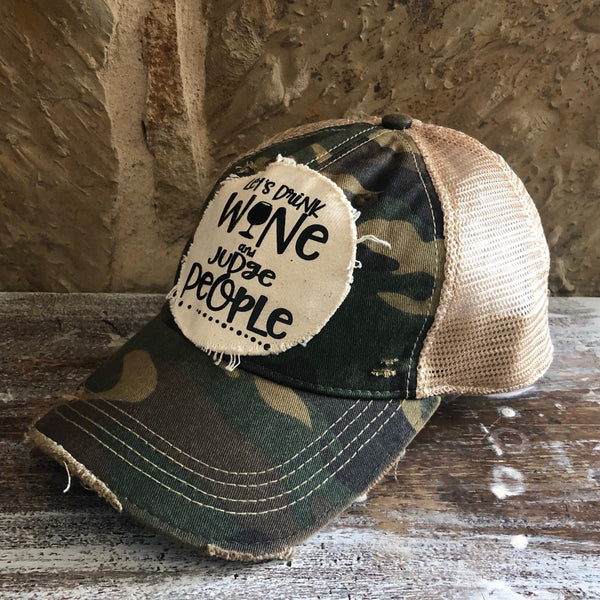 Right side view of the Let’s Drink Wine and Judge People hat by BohoGroove on a camo vintage distressed snapback trucker hat with distressed off-white patch.