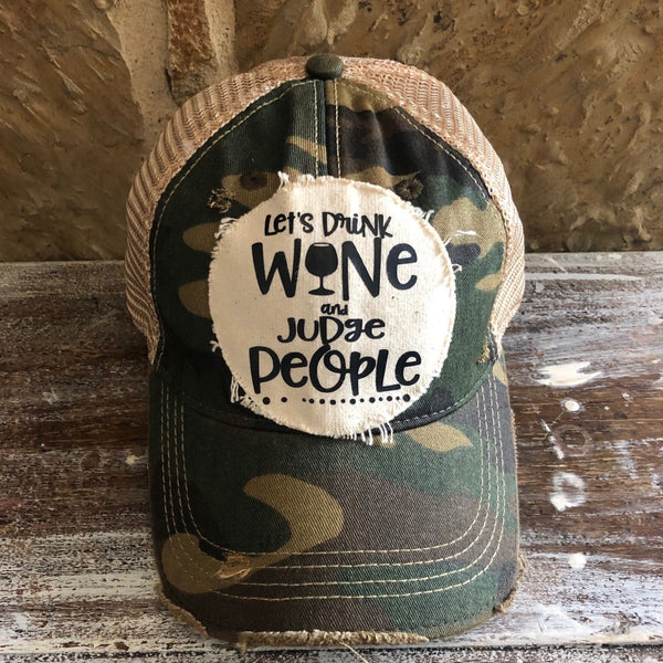 Let’s Drink Wine and Judge People hat by BohoGroove featuring whimsical black lettering with a wine glass graphic on a distressed off-white patch on a camo vintage distressed snapback trucker hat.