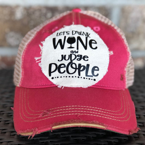 Let’s Drink Wine and Judge People hat by BohoGroove featuring whimsical black lettering with a wine glass graphic on a distressed off-white patch on a pink vintage distressed snapback trucker hat.