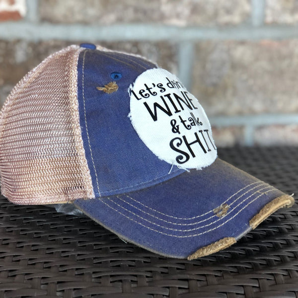 Left side view of the Let’s Drink Wine and Talk Shit hat by BohoGroove with black lettering on a distressed off-white patch on a royal blue vintage distressed snapback trucker hat.