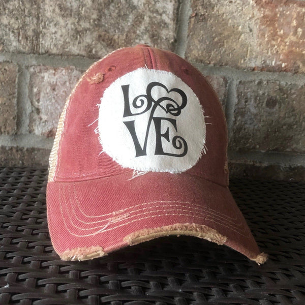 Love hat by BohoGroove with black script Love lettering and heart graphic on a distressed off-white patch on a brick red vintage distressed snapback trucker hat.