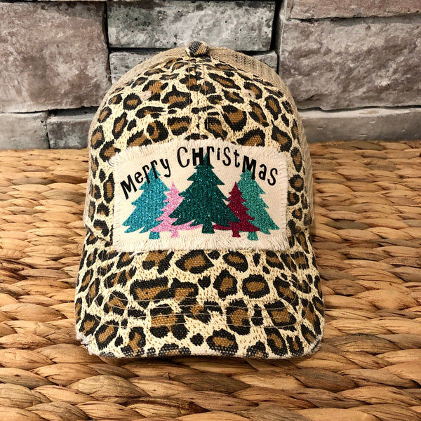 Merry Christmas hat by BohoGroove with black Merry Christmas lettering and five glitter Christmas trees in turquoise, pink, dark green, red, and mint on a distressed off-white patch on a leopard vintage distressed snapback.