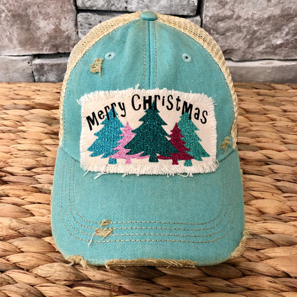 Merry Christmas hat by BohoGroove with black Merry Christmas lettering and five glitter Christmas trees in turquoise, pink, dark green, red, and mint on a distressed off-white patch on an ocean blue vintage distressed snapback.