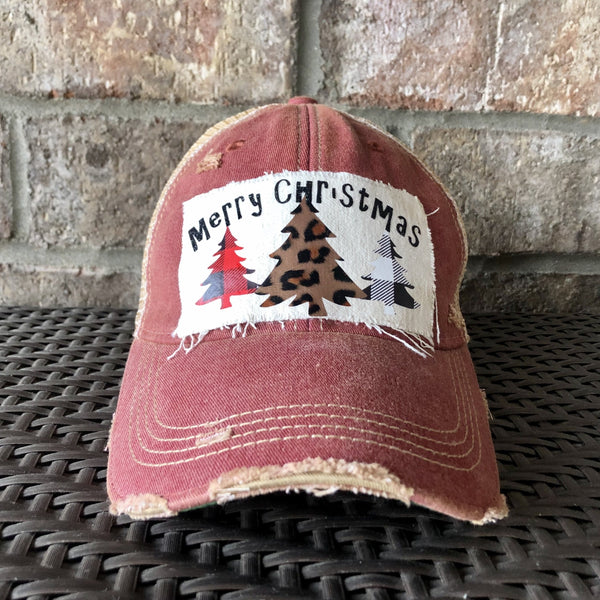 Merry Christmas Trees hat by BohoGroove with black Merry Christmas lettering and three Christmas tree graphics featuring red plaid, leopard print, and black buffalo plaid designs on a distressed off-white custom patch on a brick red vintage distressed snapback.