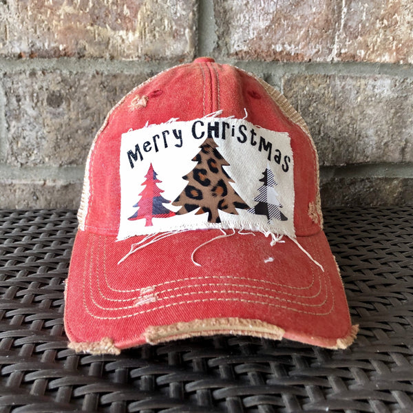 Merry Christmas Trees hat by BohoGroove with black Merry Christmas lettering and three Christmas tree graphics featuring red plaid, leopard print, and black buffalo plaid designs on a distressed off-white custom patch on a red vintage distressed snapback.