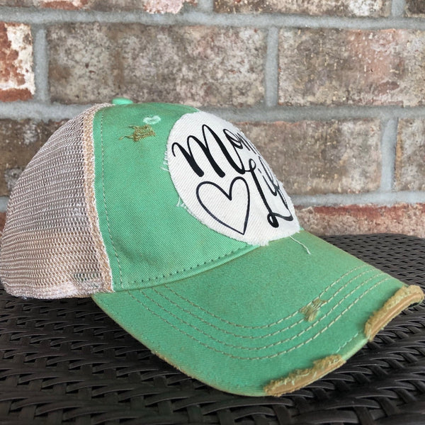 Left side view of the Mom Life hat by BohoGroove featuring black Mom Life lettering and heart graphic on a distressed off-white patch on a mint vintage distressed snapback.