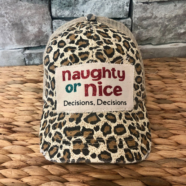 Naughty or Nice hat by BohoGroove with red and green Naughty or Nice lettering and Decisions, Decisions wording on a distressed off-white patch on a leopard vintage distressed snapback.