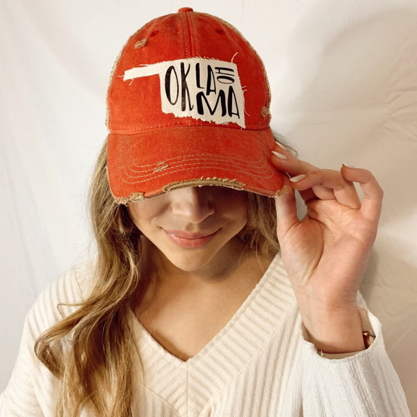 Model wearing the Oklahoma hat by BohoGroove featuring black Oklahoma lettering on a distressed off-white patch in the shape of the state of Oklahoma on a red vintage distressed snapback.