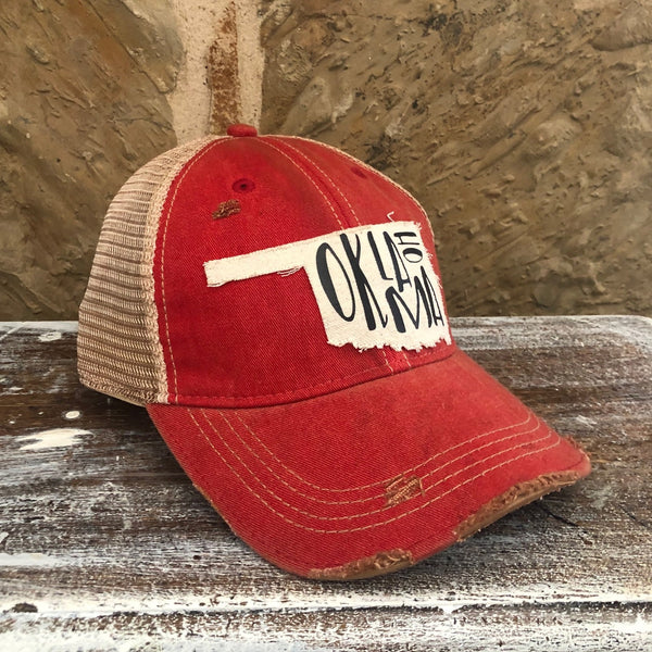 Left side view of the Oklahoma hat by BohoGroove with black Oklahoma lettering on a distressed off-white patch in the shape of the state of Oklahoma on a red vintage distressed snapback.
