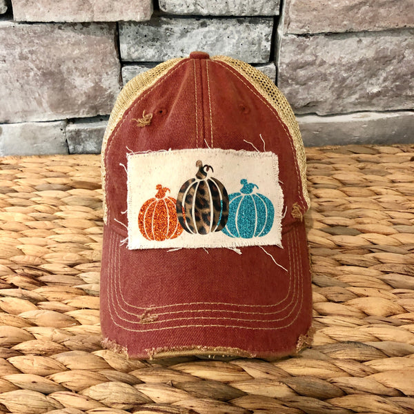 Pumpkin hat by BohoGroove featuring orange, leopard, and turquoise glitter pumpkin graphics on a cream patch on a brick red vintage distressed snapback.