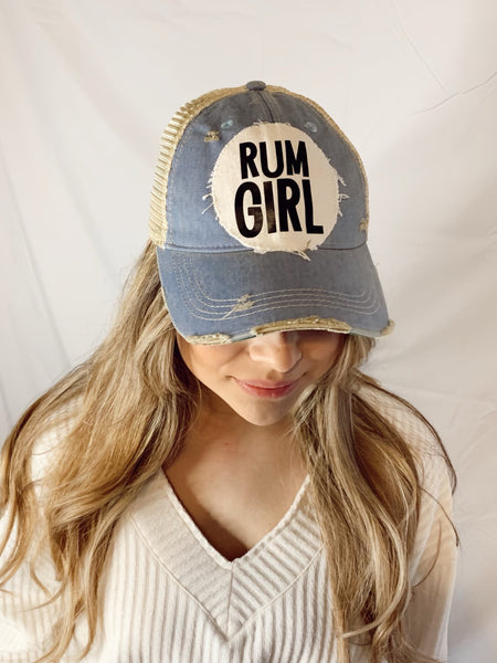 Woman wearing a light blue vintage distressed snapback trucker hat by BohoGroove featuring a distressed off-white patch with bold black Rum Girl lettering.