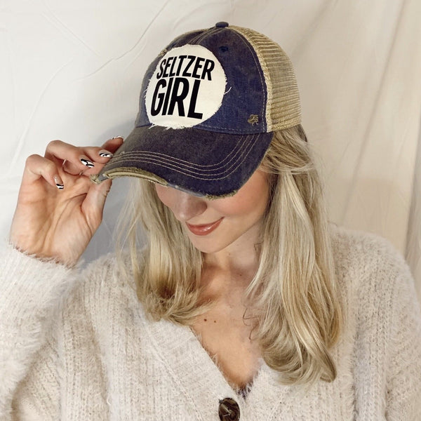 Woman wearing a Seltzer Girl hat by BohoGroove with black lettering on a distressed off-white patch on a navy blue vintage distressed snapback trucker hat.