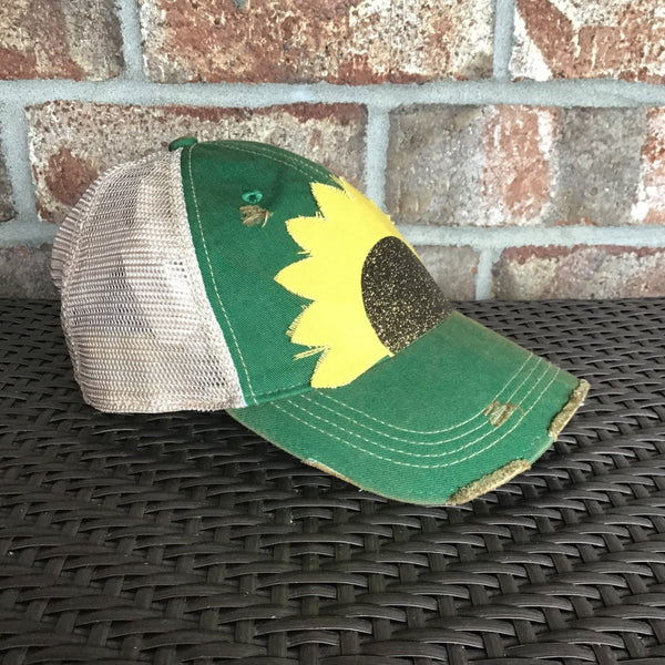 Sunflower hat by BohoGroove with yellow sunflower petals and a black glitter sunflower center on a green vintage distressed snapback left side.