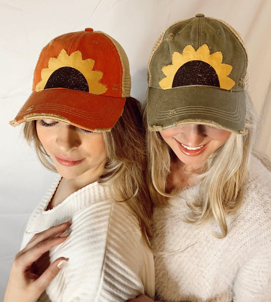 Two women modeling BohoGroove sunflower hats with yellow sunflower petals and black glitter sunflower centers on vintage distressed snapback hats.