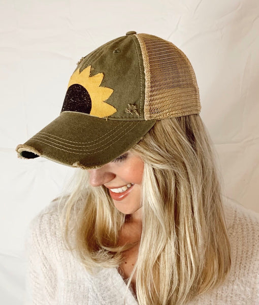 Woman modeling BohoGroove sunflower hat with yellow sunflower petals and black glitter sunflower centers on an olive  vintage distressed snapback hat.