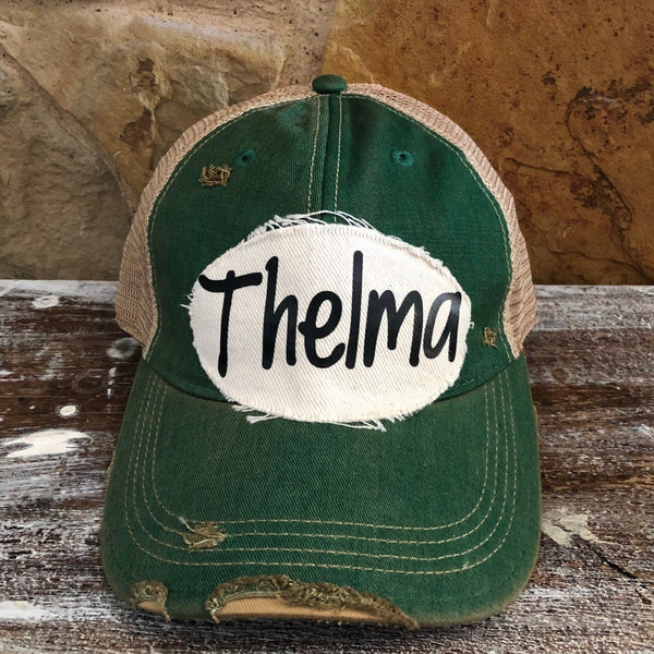 Thelma hat by BohoGroove with black Thelma lettering on a distressed off-white patch on a green vintage distressed snapback trucker hat.